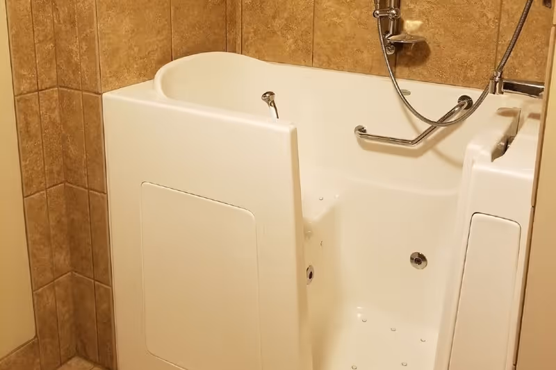 A white walk-in bathtub with a side door, grab bar, handheld showerhead, and tiled walls.