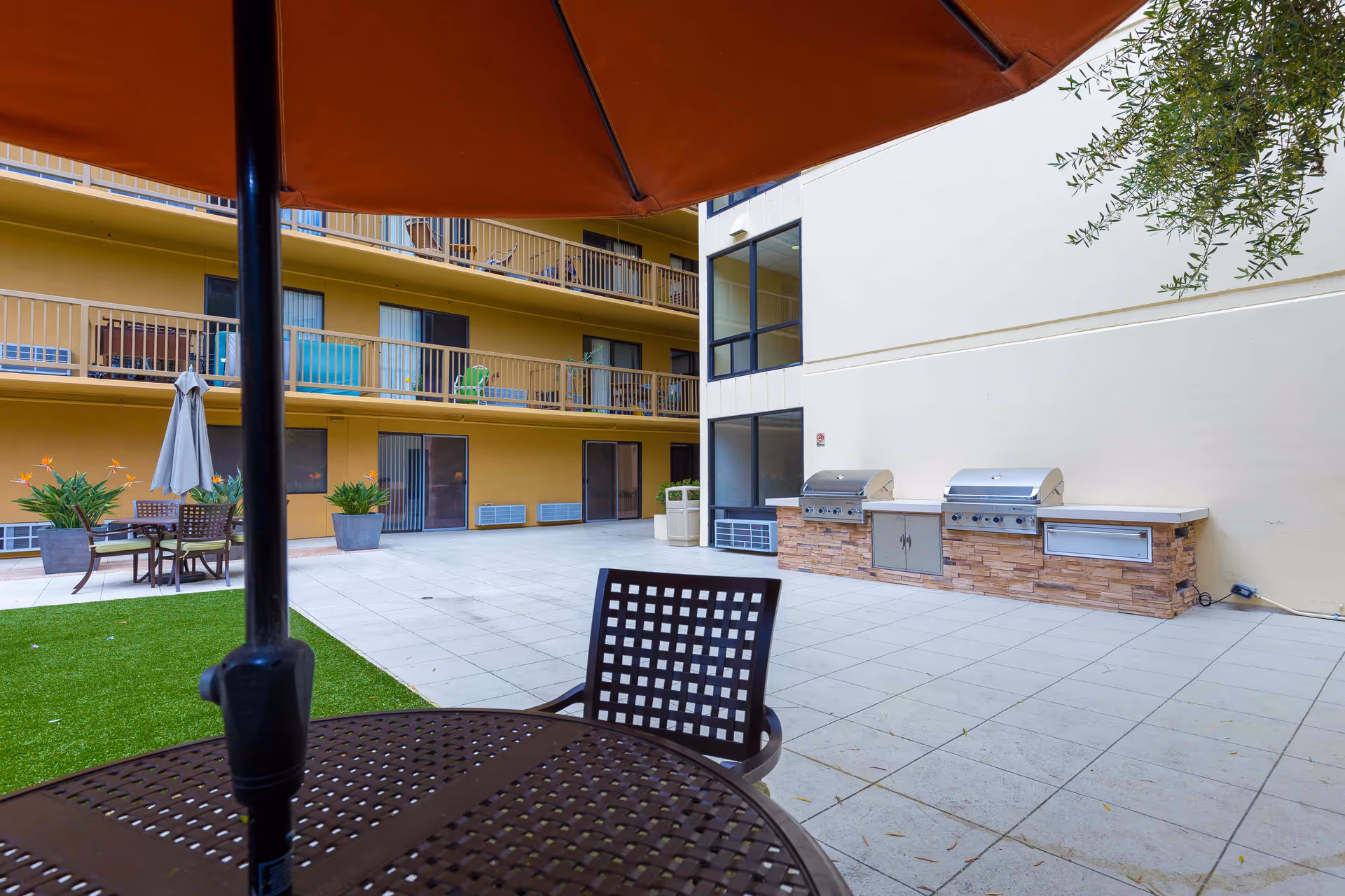 Outdoor courtyard with patio tables and umbrellas, built-in grills, and surrounding apartment balconies.