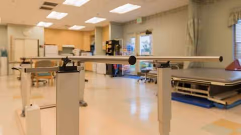 Indoor therapy area with parallel bars and medical equipment in a senior facility.