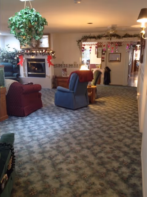 Carpeted communal living room with recliner chairs, a fireplace, hanging plants and holiday decorations.