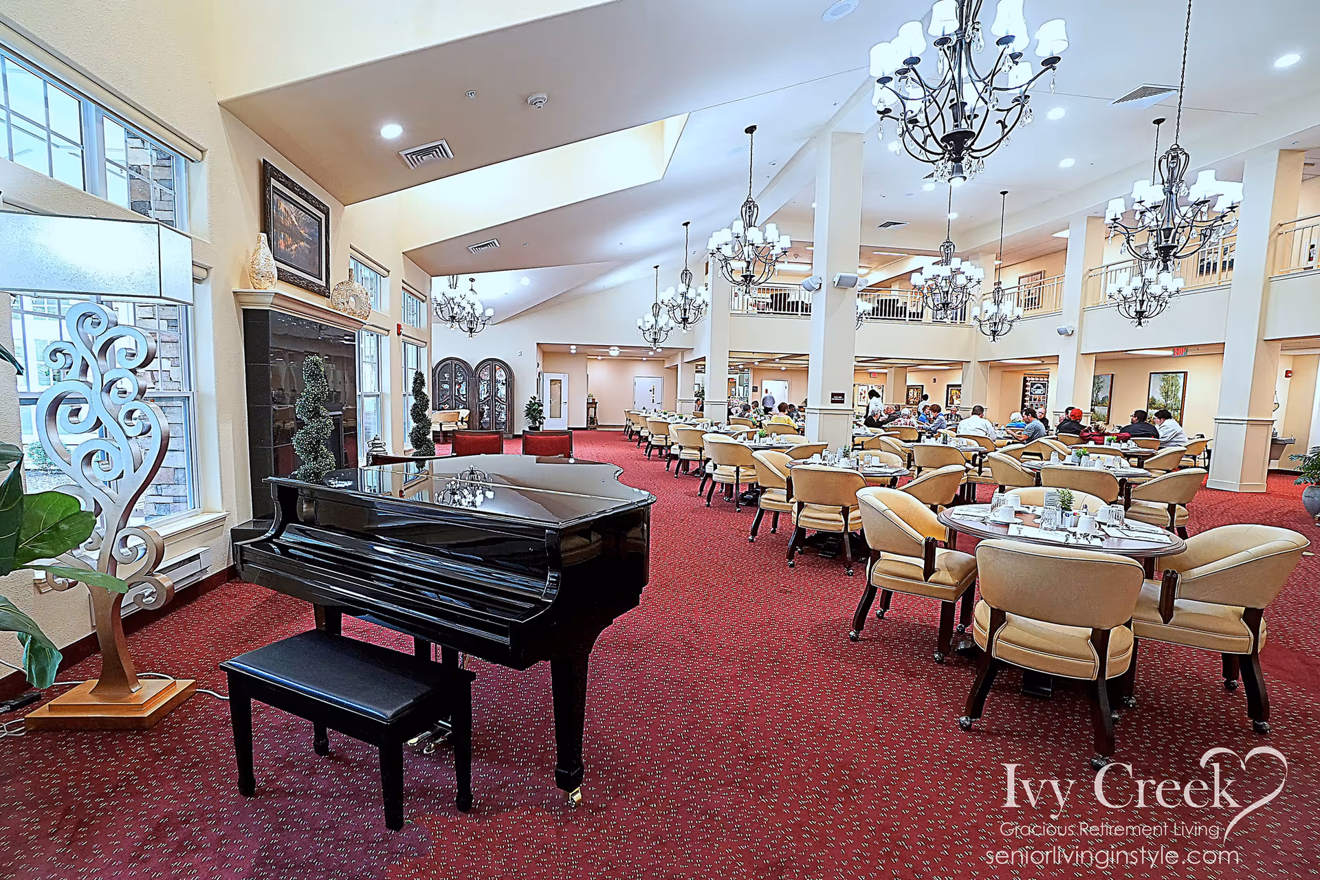 Large elegant dining room with a black grand piano in the foreground, round tables and chandeliers and residents seated in the background.