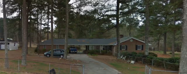 Single-story brick care home exterior with a parking area and surrounding trees.