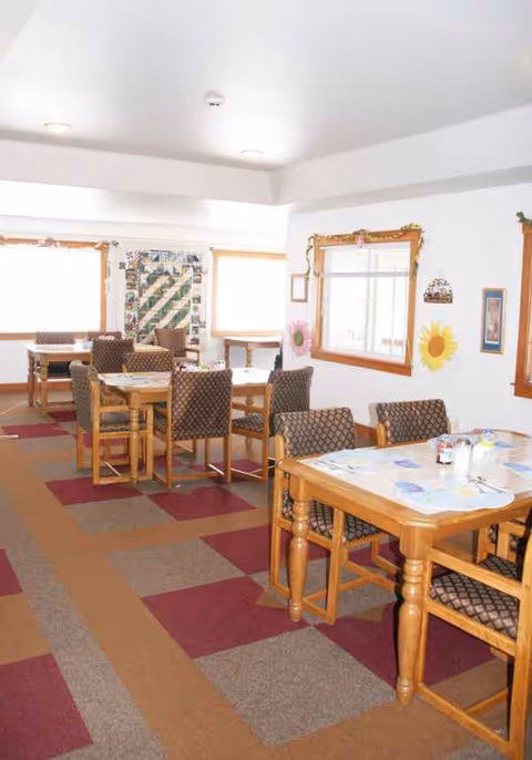 Bright dining room with wooden tables, patterned chairs, and cheerful wall decorations.