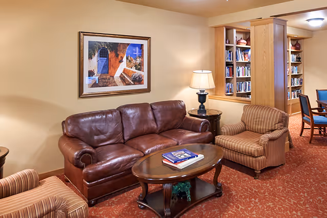 Comfortable common room with a brown leather sofa, striped armchairs, a coffee table, lamp, and bookshelves.