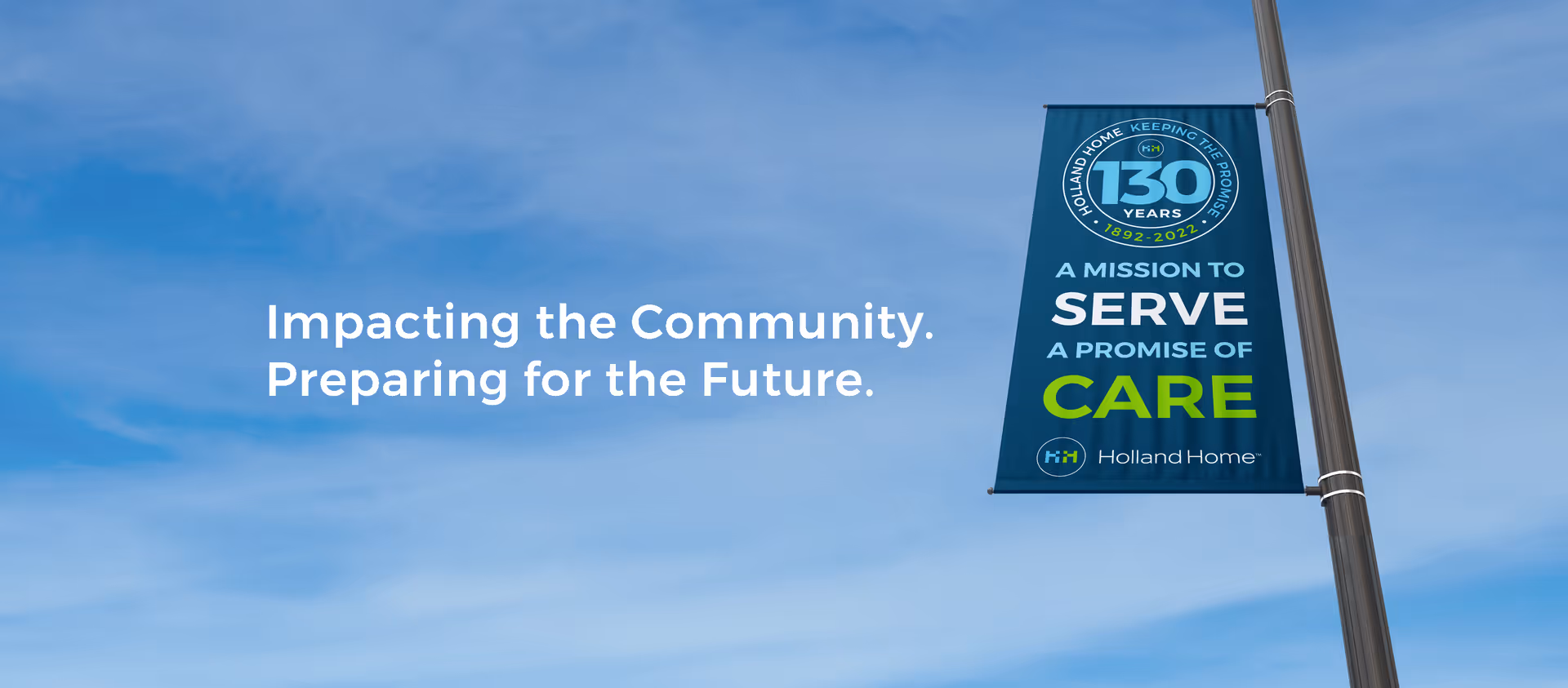 A street lamp pole with a blue banner celebrating 130 years of Holland Home from 1892 to 2022. The banner reads: 'A mission to serve a promise of care' with the Holland Home logo at the bottom. The sky is clear with a few clouds.