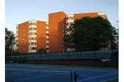 Brick senior living facility with a fence and tennis court in front.
