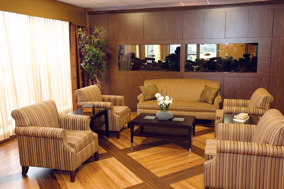 Communal lounge with matching striped armchairs and a sofa arranged around a dark coffee table on a patterned wood floor.