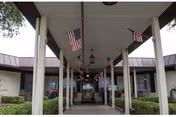 Covered entrance walkway to a building with multiple American flags hanging from the ceiling. The building has large windows and bushes lining the walkway.