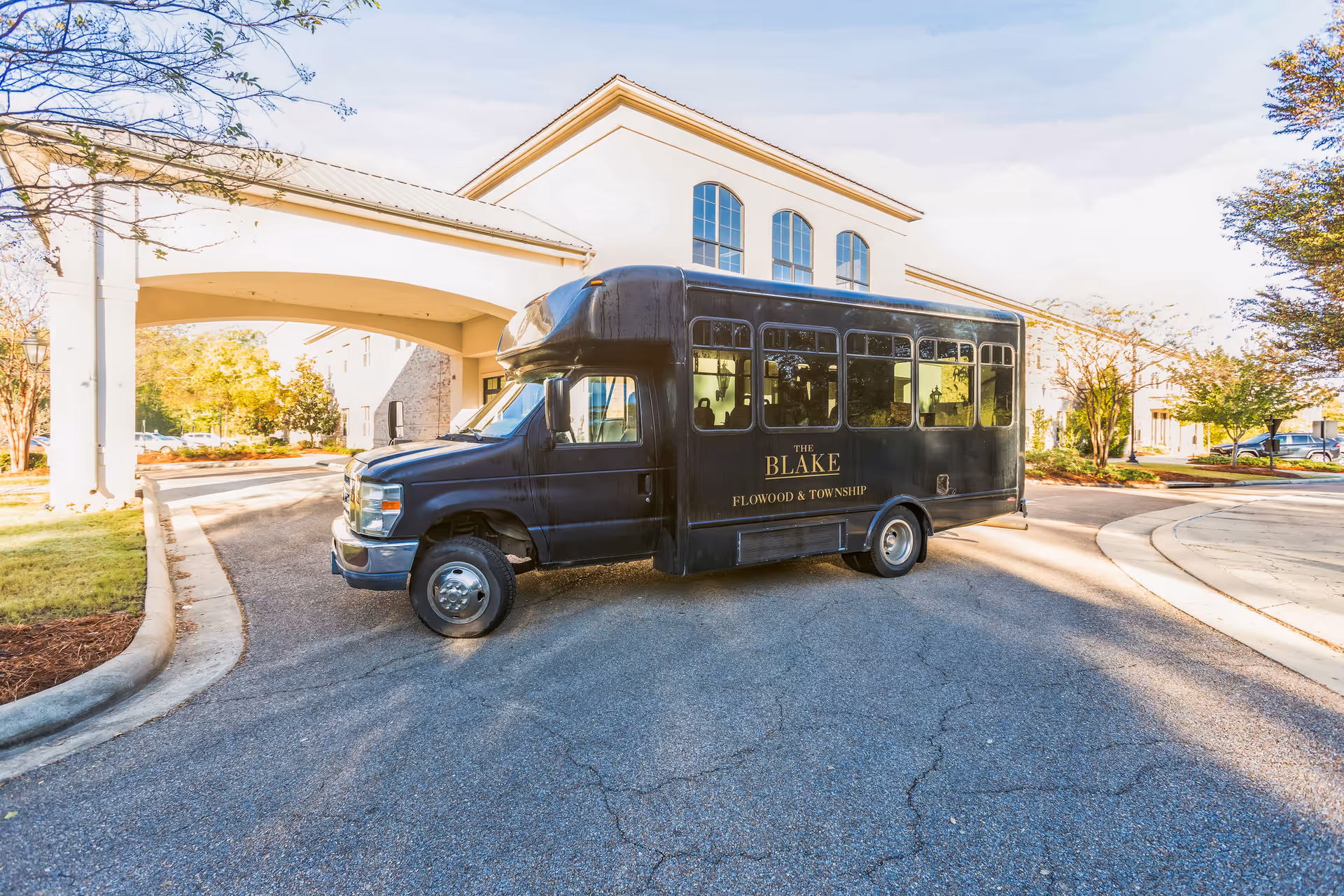 A black shuttle bus labeled "The Blake Flowood & Township" parked under the covered entrance of a senior living building.