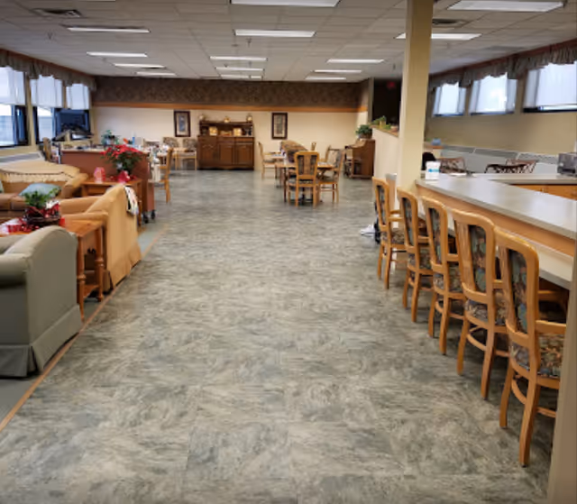 Open communal dining and lounge area with tables and chairs, a long counter with barstools on the right, and sofas on the left.