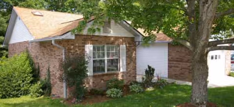 Single-story brick retirement residence with front yard, shrubs, and a large tree.