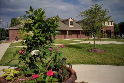 Exterior view of Home Sweet Home RCFE with brick building, lawn, trees, and potted flowers.