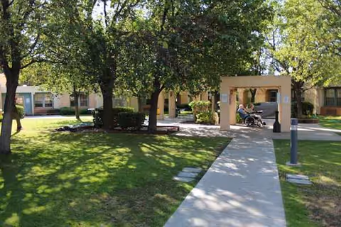 Exterior view of a senior living facility with a walkway, trees, and a front entrance.