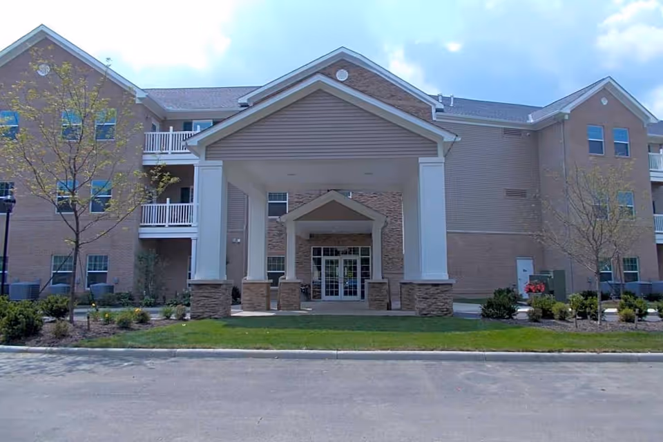 Front entrance of a three-story brick senior living building with a covered portico and landscaped grounds.