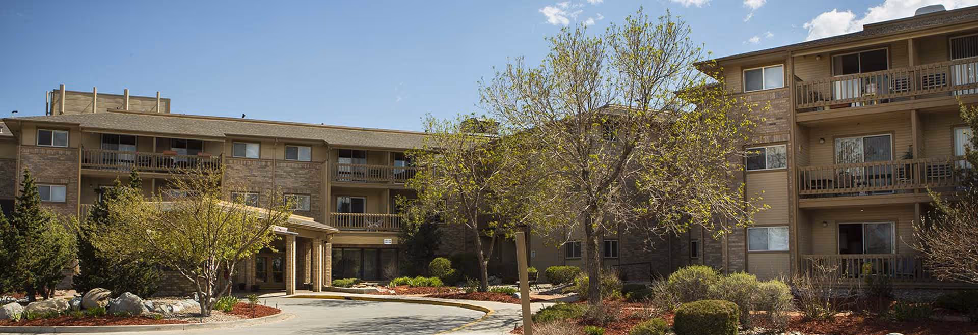 Exterior view of a multi-story senior living facility named Viewpointe, featuring balconies, trees, shrubs, and a circular driveway under a partly cloudy sky.