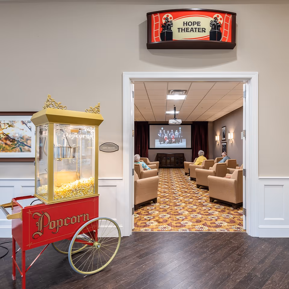 Entrance to the 'Hope Theater' with a vintage popcorn cart in the foreground and residents seated inside watching a movie.
