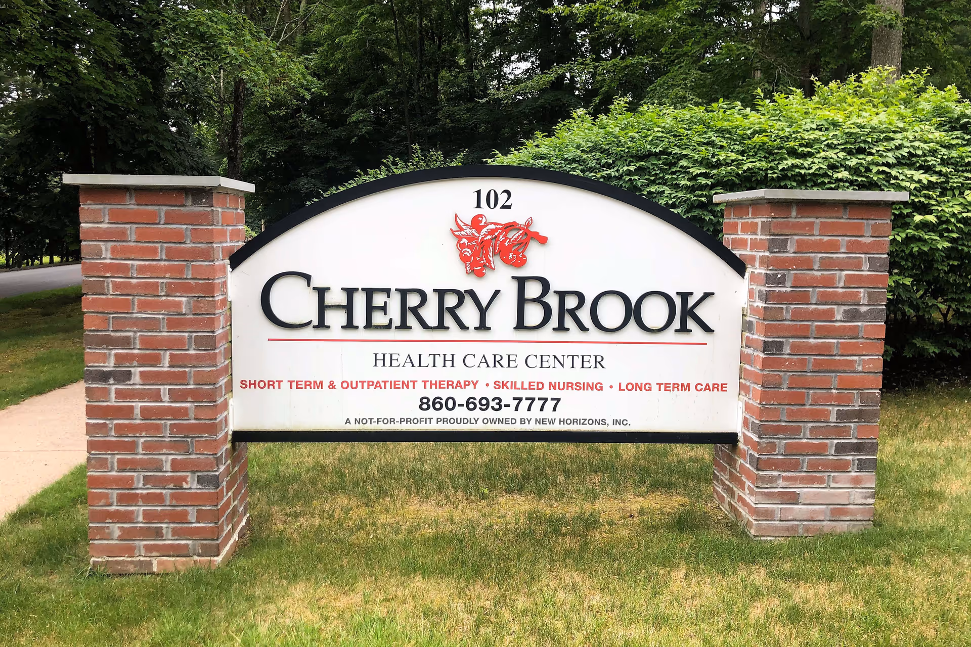 A large outdoor sign for Cherry Brook Health Care Center, supported by two brick pillars, surrounded by grass and greenery with trees in the background.