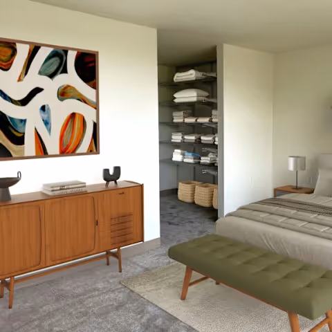 Bedroom in a Bethany House senior living facility with a bed, green tufted bench at the foot, a wooden dresser, wall art, and an open linen closet.