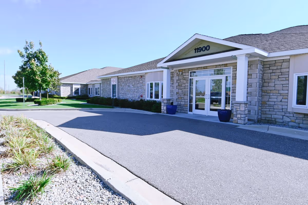 Front entrance of a single-story building with a stone facade, double glass doors under a portico showing the number 11900.