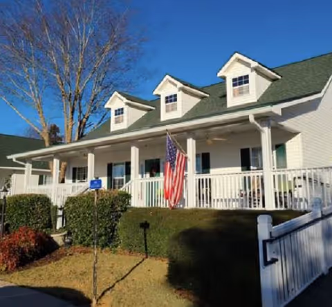 White Magnolia Hills facility with a covered porch, railing, and American flag outside.