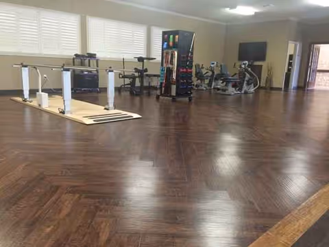 Indoor rehabilitation gym with wooden floors, exercise equipment, and a wall-mounted TV.
