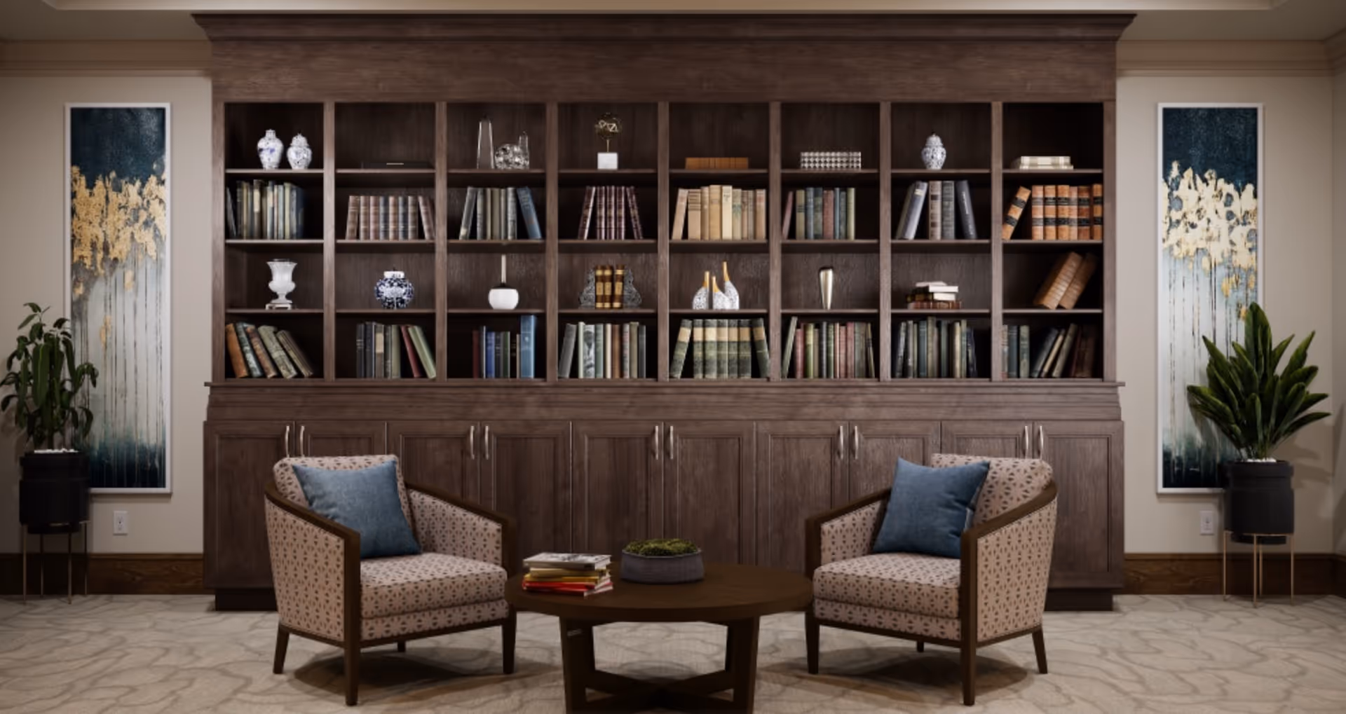 A cozy seating area with two patterned armchairs featuring blue cushions facing a round wooden coffee table with books and a small plant. Behind the seating area is a large wooden bookshelf filled with books and decorative items. On either side of the bookshelf are tall plants in black pots and vertical abstract paintings with blue, white, and gold tones. The room has a neutral carpet and beige walls.