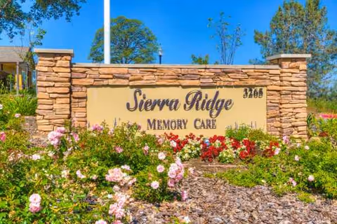 Stone entrance sign reads Sierra Ridge Memory Care with colorful flower beds in front.