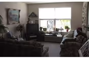 Cozy living room with floral sofas, a TV cabinet, and a large window with plants on the windowsill.