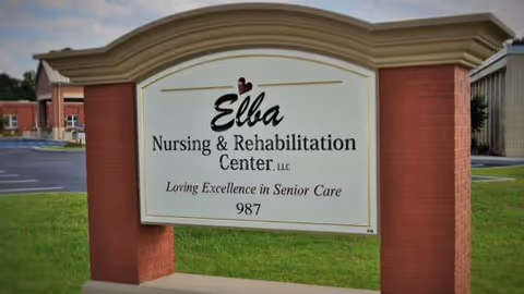 A brick-framed roadside sign that reads "Elba Nursing & Rehabilitation Center" standing on a lawn in front of the facility.