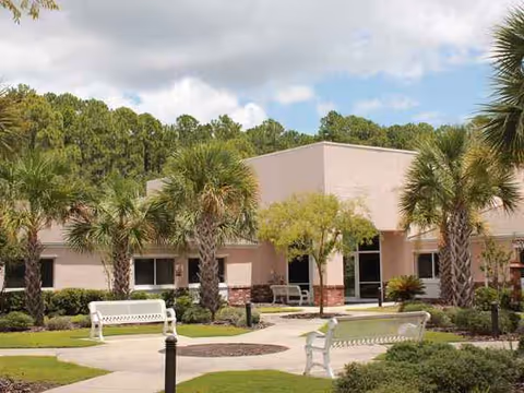 Exterior view of Isle Health and Rehab Center with palm trees and white benches.