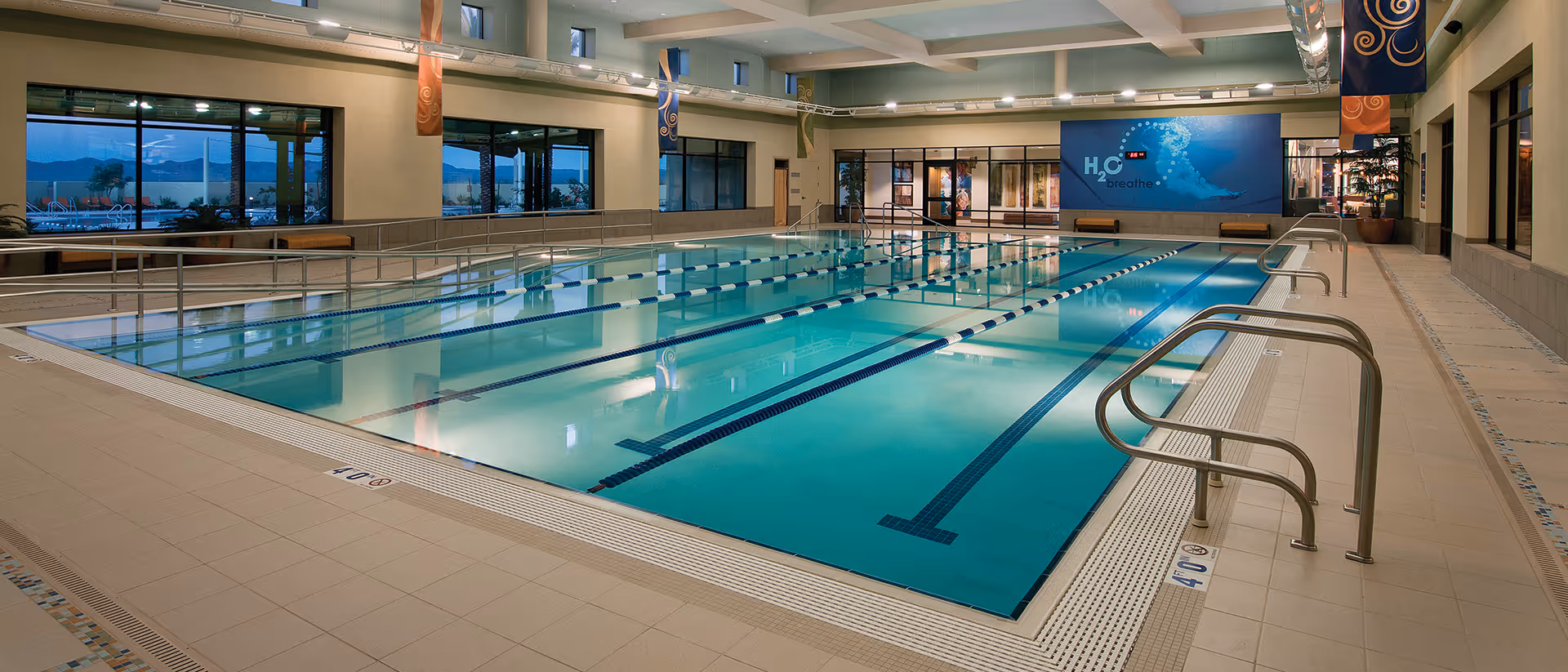 Spacious indoor lap pool with marked lanes, handrails, large windows, and a mural on the far wall.