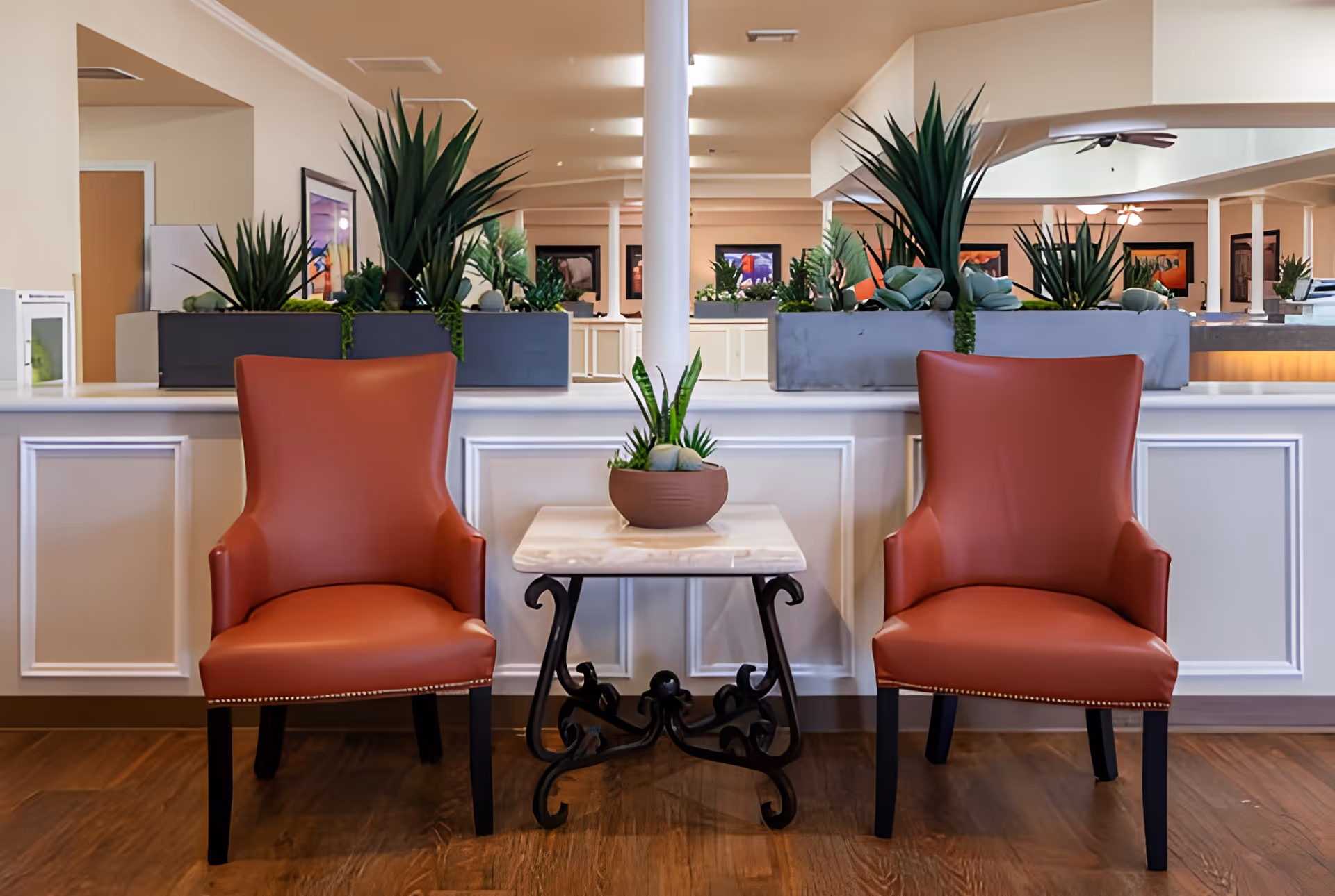 Two red armchairs flank a small marble-top table with a potted plant in a well-decorated lobby seating area with planters behind.