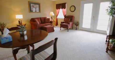 Cozy living room with burgundy sofa, chairs, round table, and natural light.