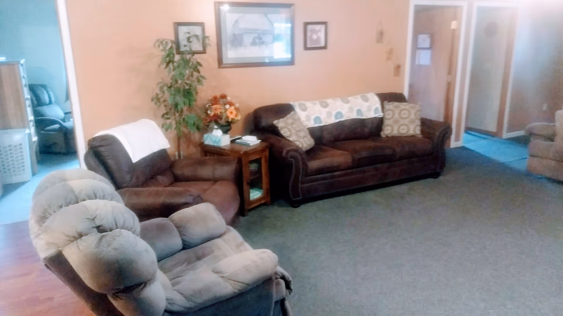 A living room with several upholstered recliners and a sofa arranged around a side table against a peach-colored wall.
