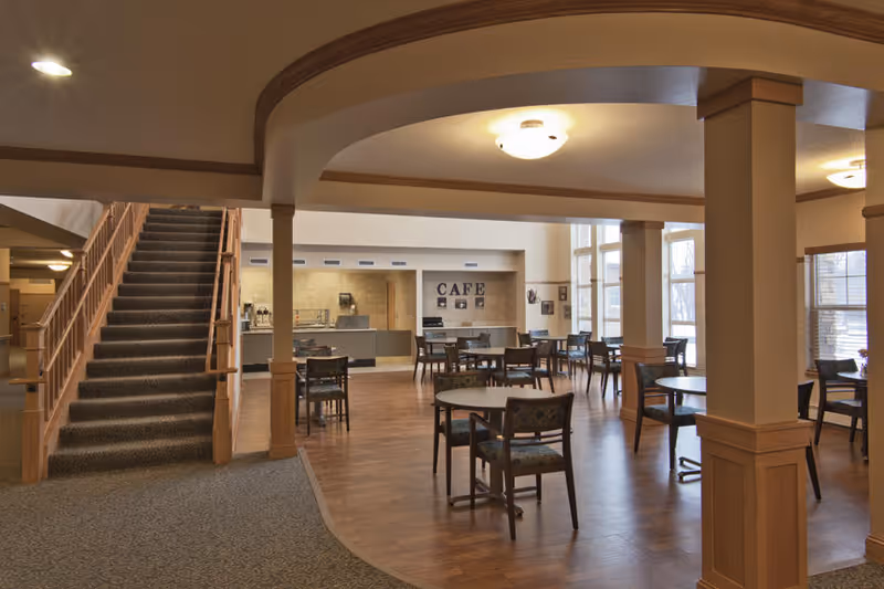 Open dining area with round tables and chairs, a café counter on the far wall, and a carpeted staircase to the left.