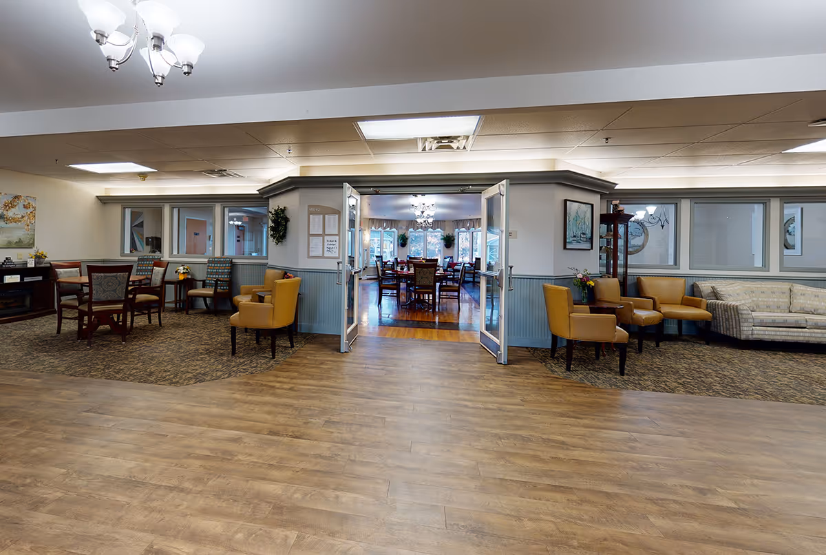 Spacious senior living common area with seating and open double doors leading to a dining room.