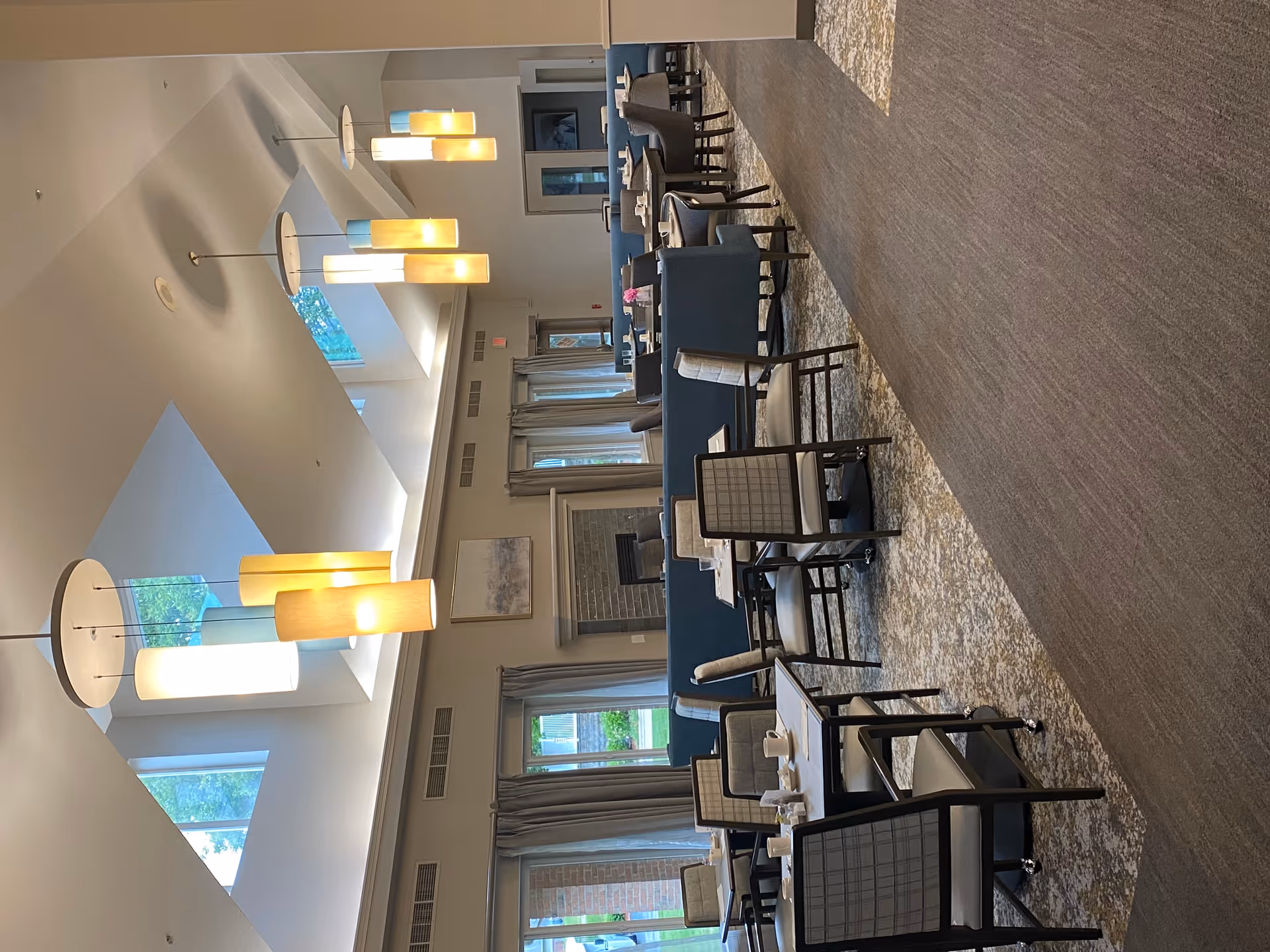 Bright dining room with long tables, chairs, and warm pendant lights.