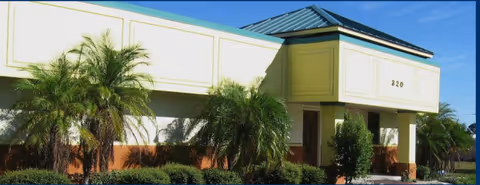 Exterior view of Tropical Living Club 2 facility with palm trees and entrance.