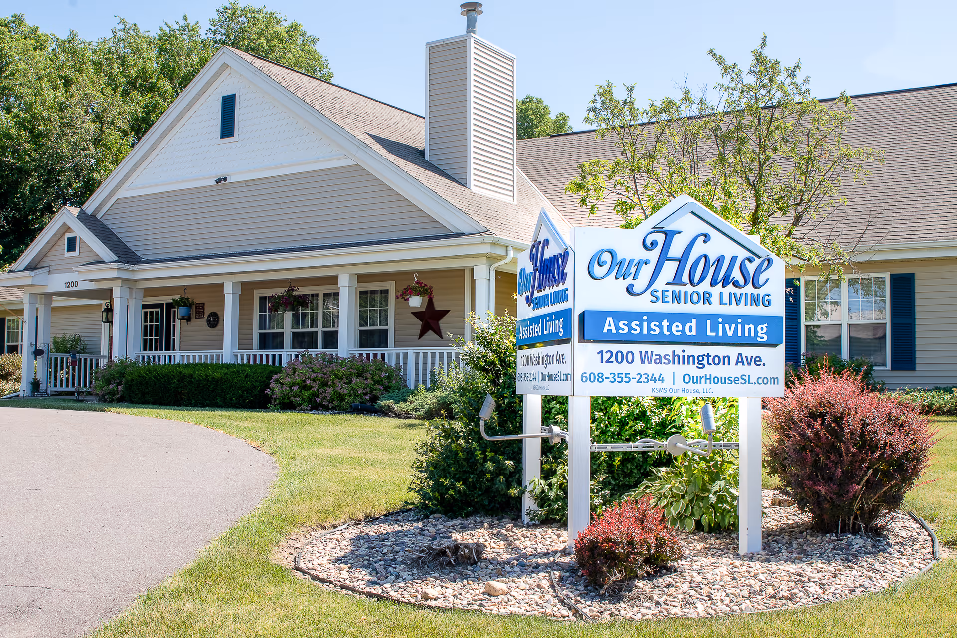 Front of a beige assisted living building with a lawn and a large 'Our House Senior Living - Assisted Living' sign at the driveway.