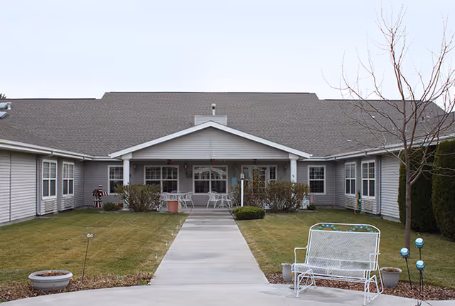 Single-story senior living building with a central covered porch, walkway, lawn, and outdoor seating.