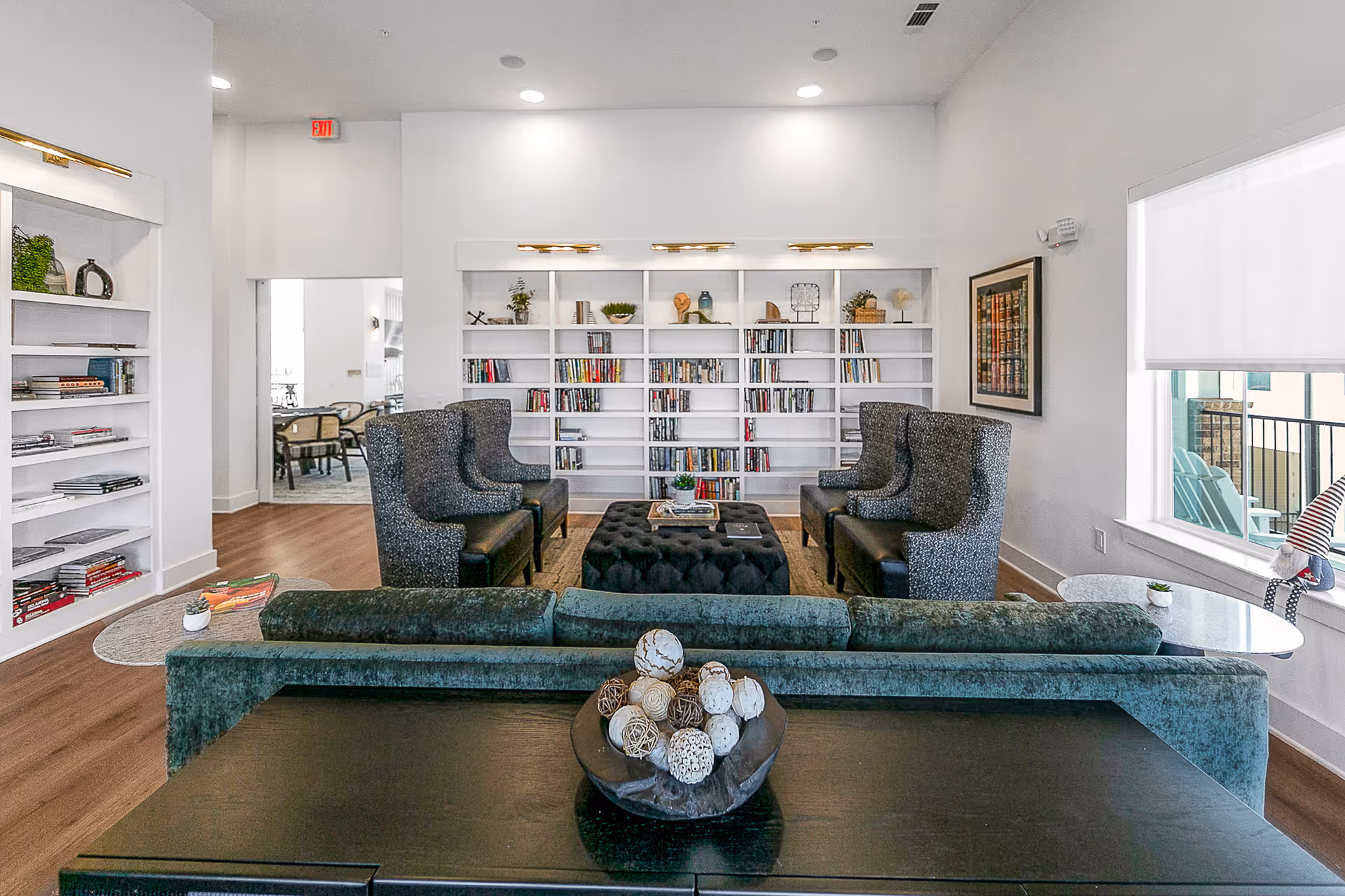 Bright, modern lounge with built-in bookshelves, a velvet sofa, wingback chairs and a central tufted ottoman.