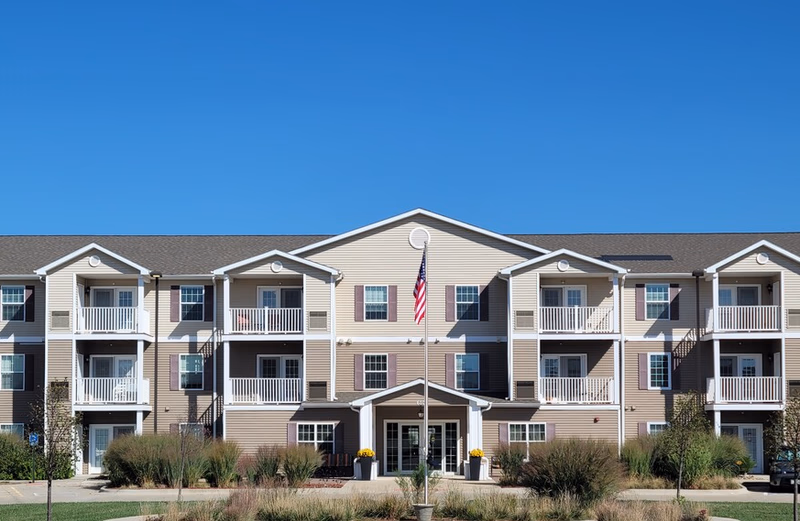 A multi-unit senior living building with balconies, central entrance, and a flagpole.