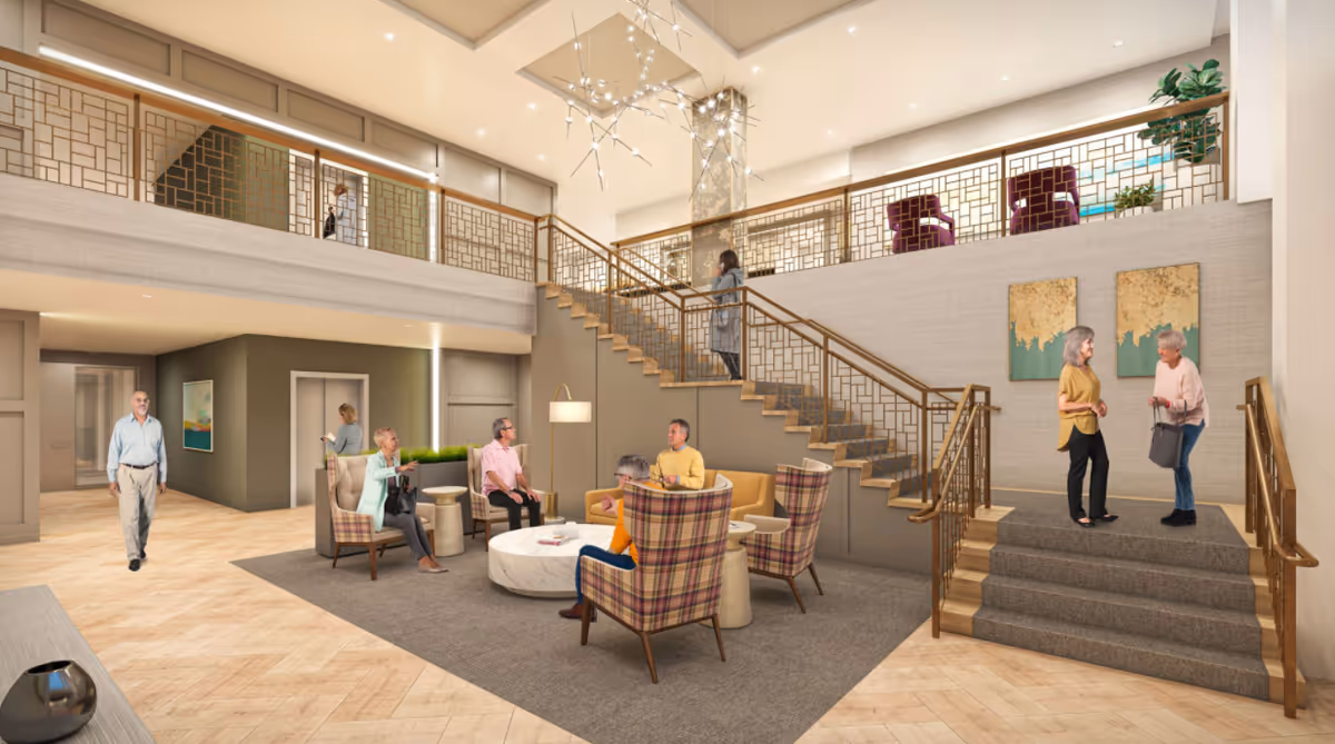 Two-story senior living lobby with a seating area, central staircase, and residents socializing.