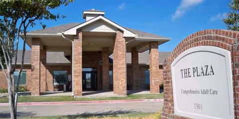 Brick-front senior living facility entrance with a curved sign reading The Plaza.