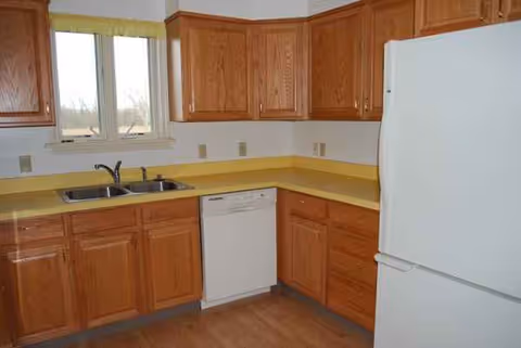 Bright L-shaped kitchen with wooden cabinets, yellow countertops, sink, dishwasher, and fridge.