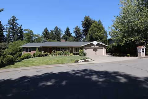 Single-story care home with driveway, green lawn, and trees in a suburban setting.