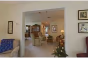 View through an interior doorway into a living room area with armchairs, a coffee table, and lamps. The room is decorated with framed artwork on the walls and plants, creating a cozy and inviting atmosphere.