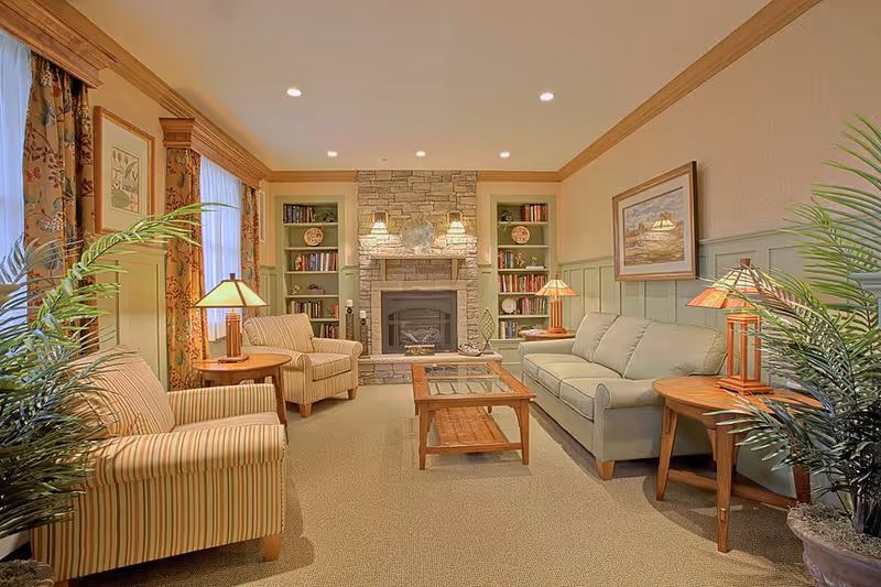 Cozy lounge with sofas and armchairs arranged around a coffee table in front of a stone fireplace flanked by built-in bookshelves.