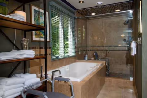 Modern senior living bathroom with tub, walk-in shower, and shelves of towels.