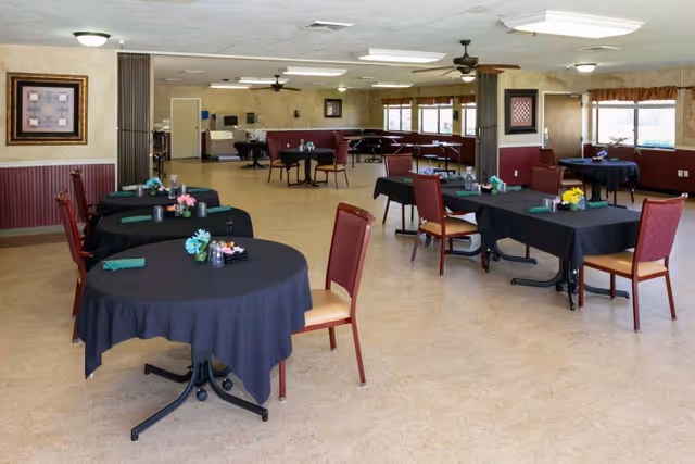 Dining room with several round and rectangular tables set with black tablecloths, centerpieces, and red chairs.